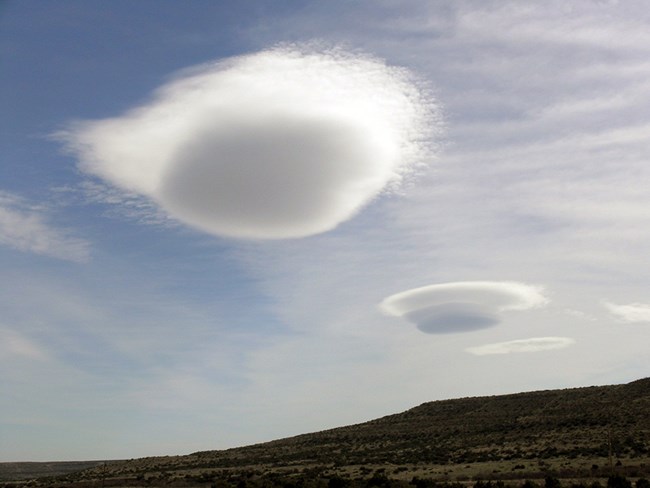 Two large circular clouds in the sky over a desert hill