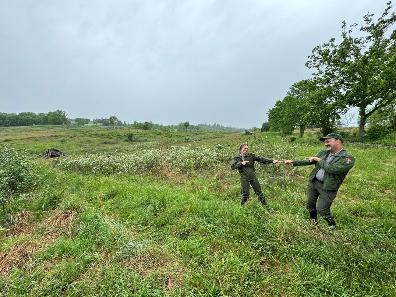 Two people in NPS uniform standing in a meadow, pointing at each other