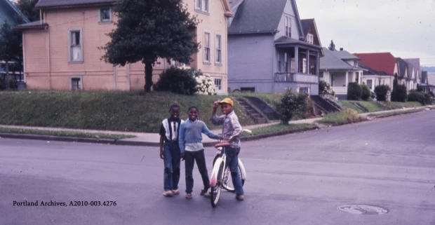 Children posing for photo with bike 3 African American boys stand around a bicycle in a neighborhood road.