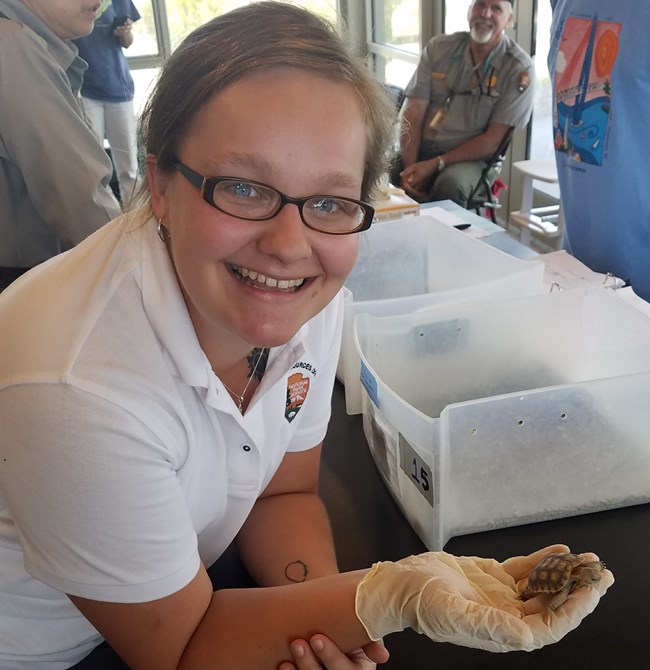 A photo of Allie Petersen in the field, holding up a small turtle