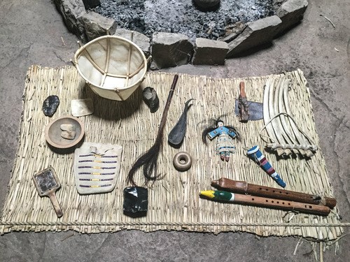 Various Native American supplies on a mat, including a bowl, flutes, bag, doll, brush, and tools at Knife River Indian Villages National Historic Site