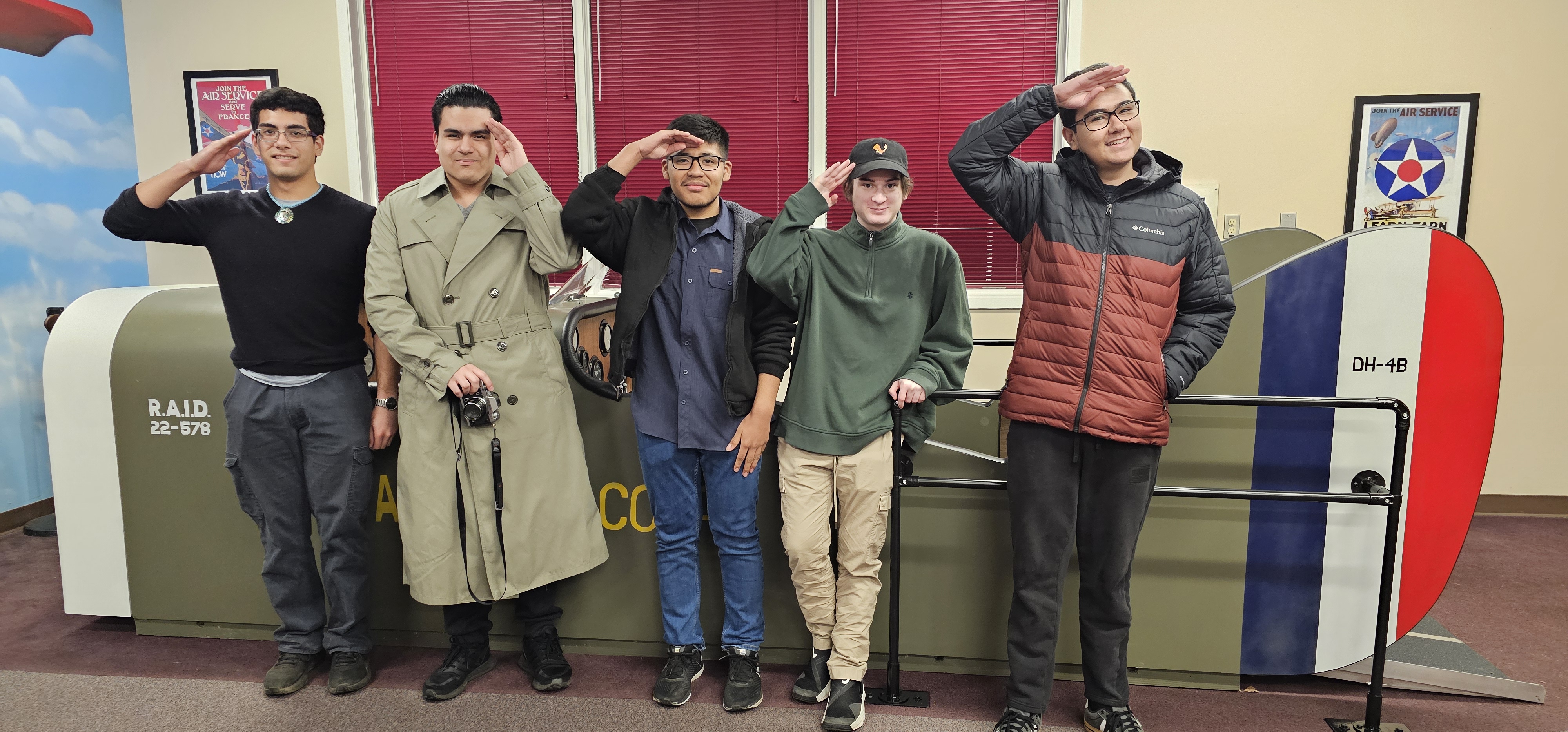 Five high school students stand in front of the aircraft model, saluting.