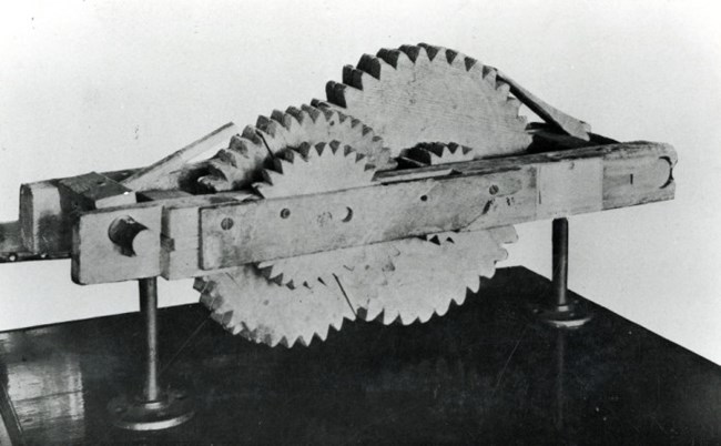 Odometer A black and white image of a piece of machinery constructed out of wood.