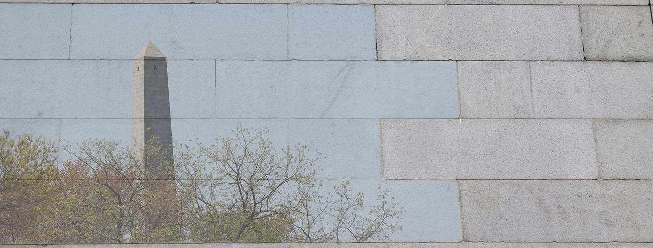 Photo of granite blocks, some of which are overlayed with a photo of the top half of the Bunker Hill Monument peaking out from trees.