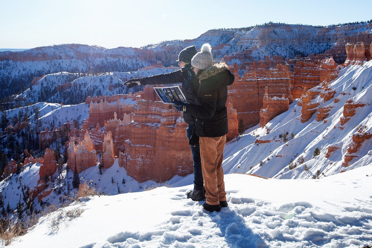 two people stand in snow above Bryce Canyon's Amphitheater pointing in the distance