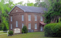 A two story brick church surrounded by live oaks