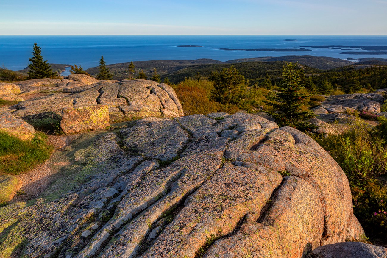 Landscape photo with pink granite boulders in foreground and open ocean with islands in distance