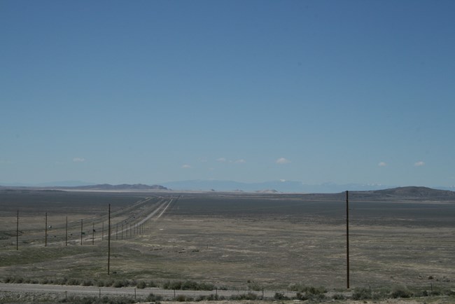 A highway cuts through a flat desert that stretches out to the horizon.