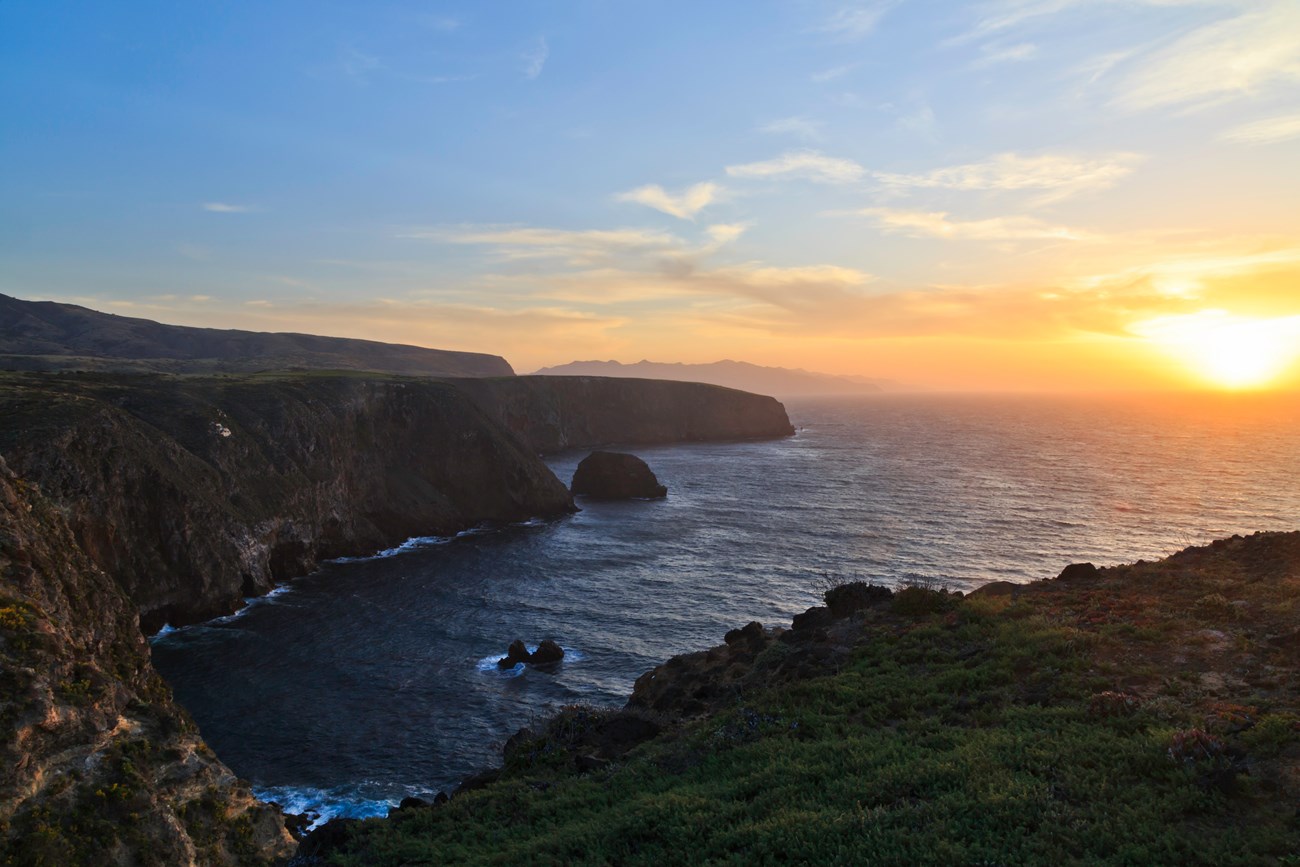 Landscape of steep coastal cliffs at sunset, islands receding in distance