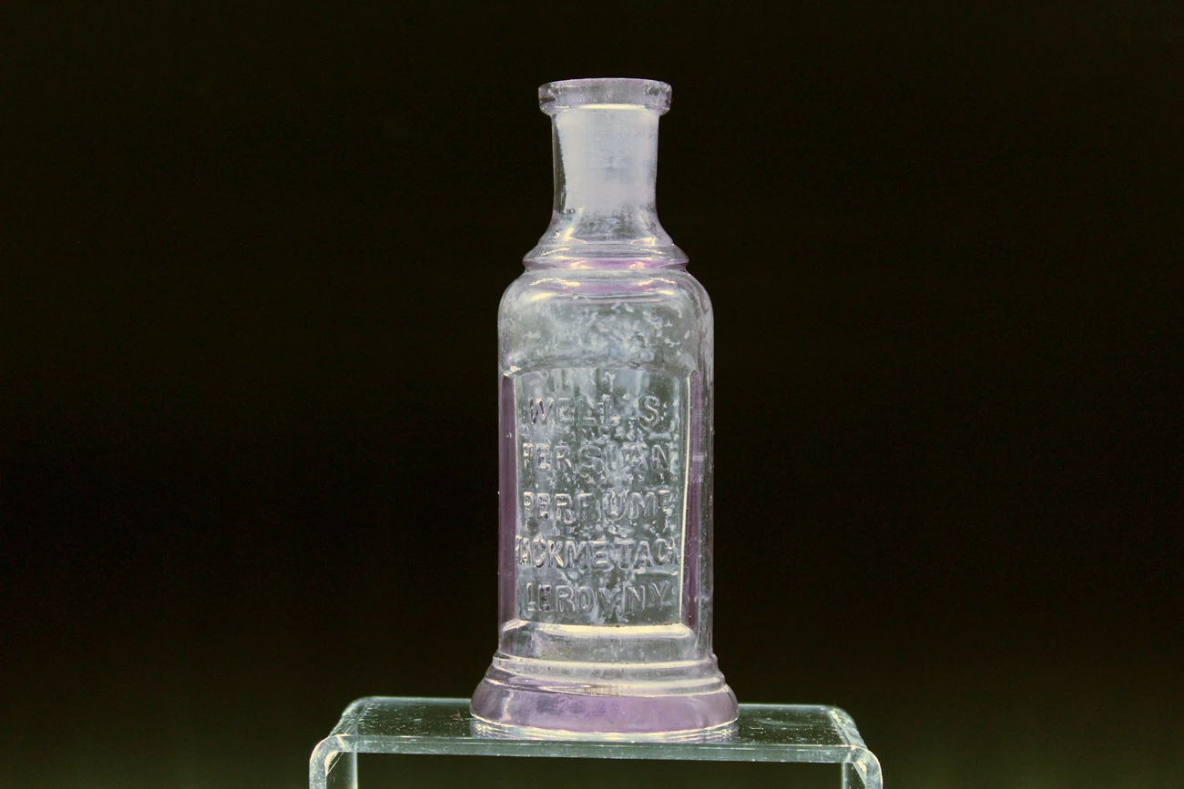Perfume Bottle Small glass bottle with inscription sits on acrylic stand.