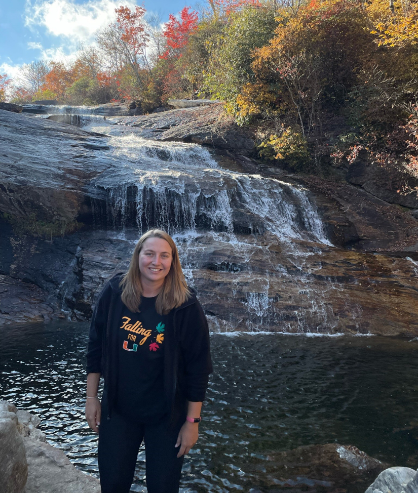 A person in a sweatshirt and jeans stands next to a waterfall.