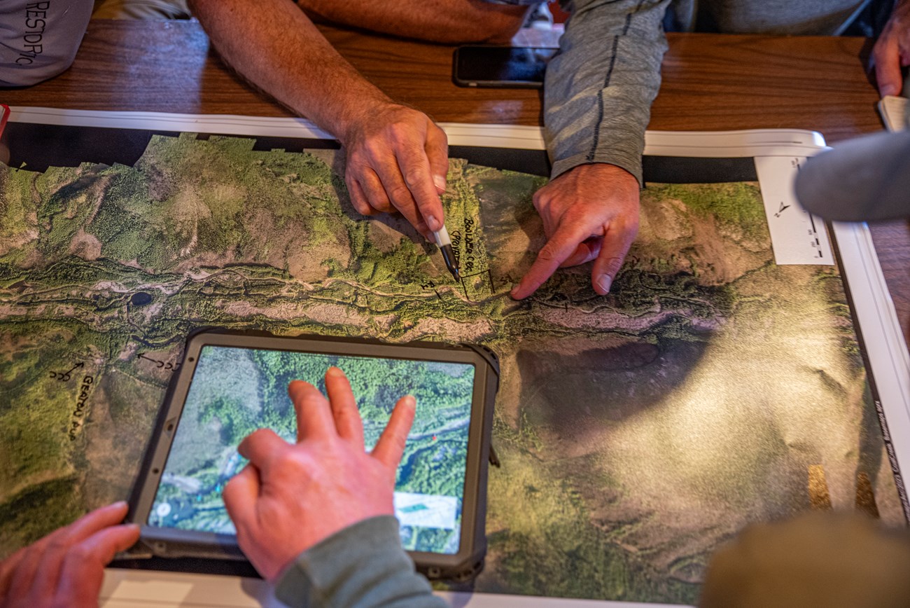 people use a printed satellite map and a digital satellite map on a tablet to plan