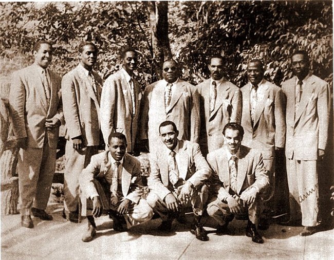 Ten afro latino men posing for a picture in suits.