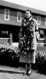 A women wearing leis around her neck stands with her hands in her pockets.