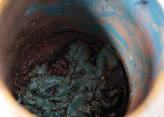 Close-up photo looking into the paint can, which has globs of hardened blue paint at the bottom.