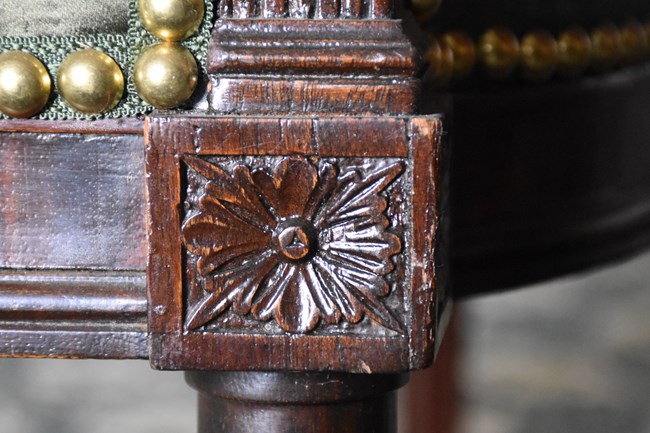A detail of furniture ornamentation. A flower is carved into mahogany wood.