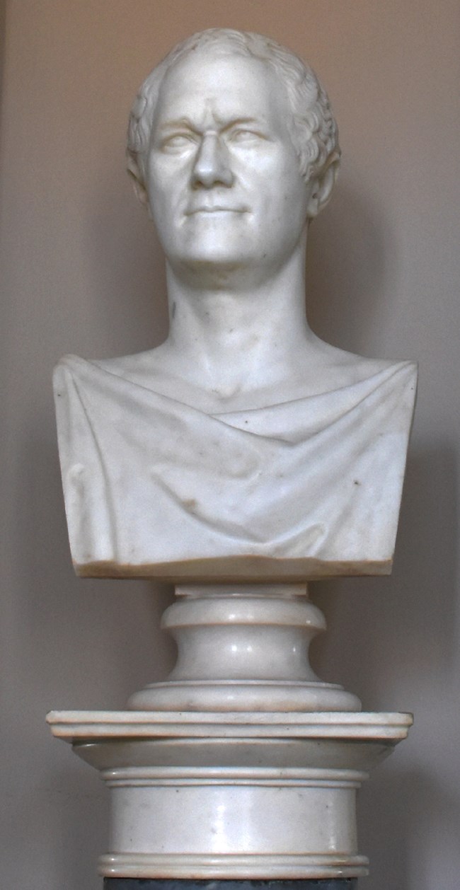 A white marble bust of Alexander Hamilton wearing a draping robe.