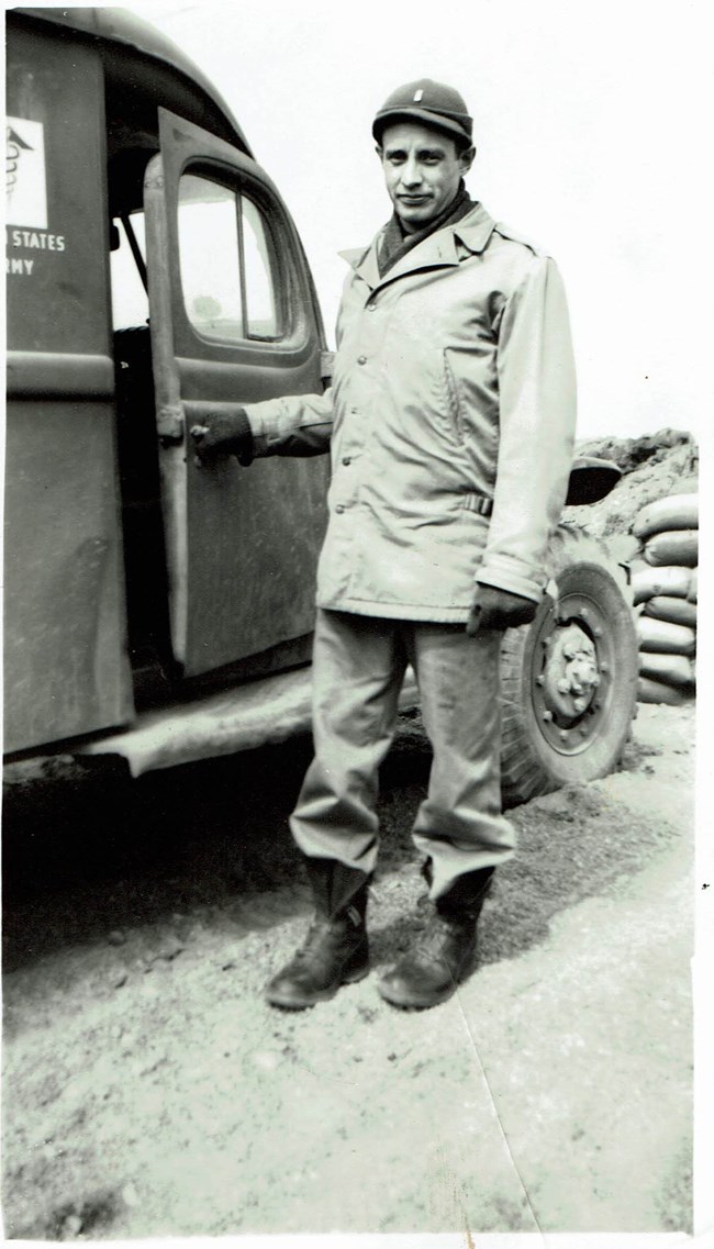 Black and white photo of a man standing beside a vehicle