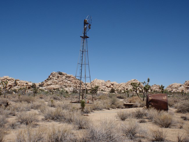 Desert Queen Well A windmill and a rusty barrel surrounded by a desert landscape