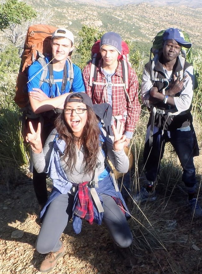 a group of 4 young adults wearing backpacks on a trail