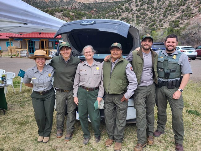 Six park rangers stand together and smile during an outdoor event.