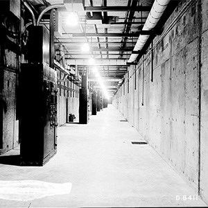 A black and white photo of a large, narrow, lit concrete hallway.