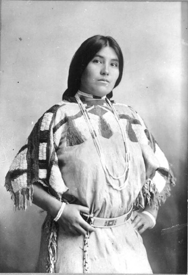 Black and white portrait of young indigenous woman in beaded dress and belt.