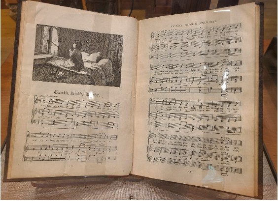 Open book with etching of child in a prayer- like gesture looking out window and underneath “twinkle twinkle little star” followed by music notes