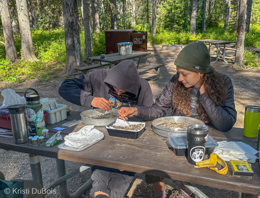 Emme sorting Moths Two people sit at a picnic table and use tweezers to sort moths into a metal pan.