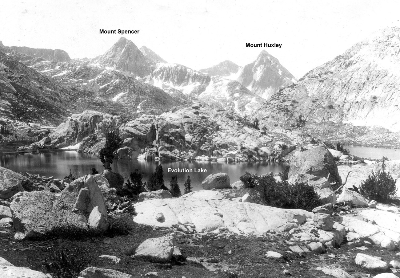 Black and white photo of a rocky lake basin, looking across lake toward rugged peaks.