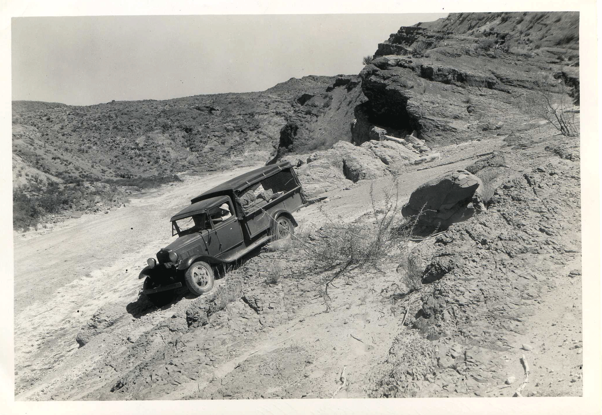 Photo of a truck driving through the desert on a dirt road.