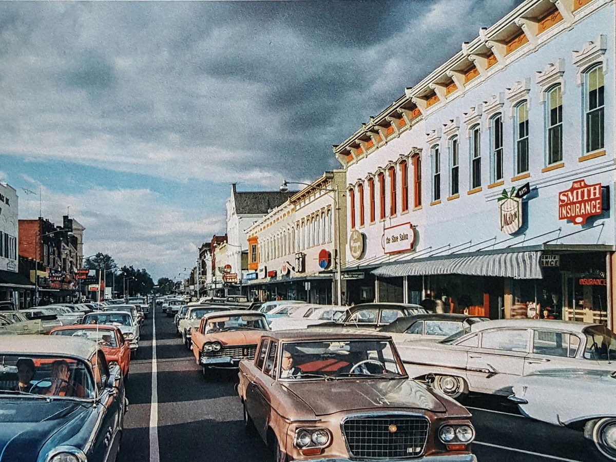 Washington Street 1965 Looking down bumper to bumper traffic on a city street with brick building store fronts and angle parking.