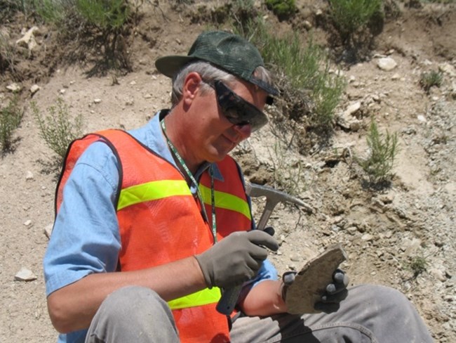 Figure 4 flfo a person sitting on the ground tapping a rock with a rock hammer