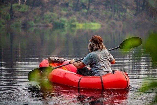 A woman paddles an inflatable boat on a lake.