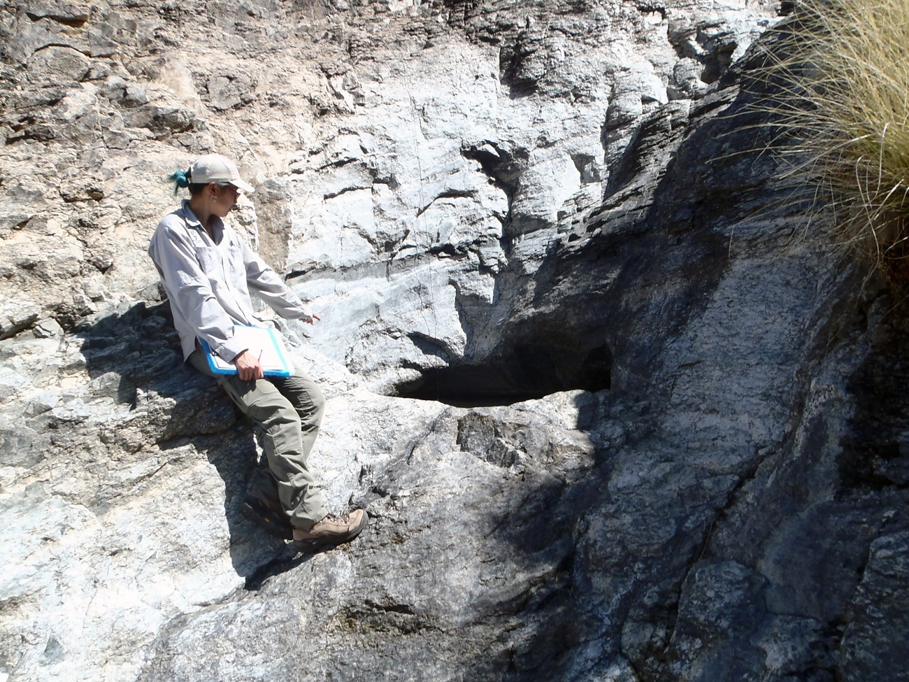 Javelina Tank tinaja A person standing on a rock lip of a steep cliff next to a water filled depression in the rock of the cliff.