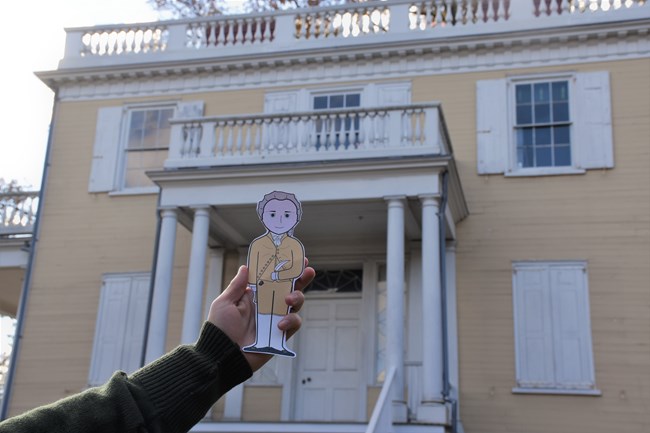 A cartoon cutout of Hamilton in front of a yellow house.