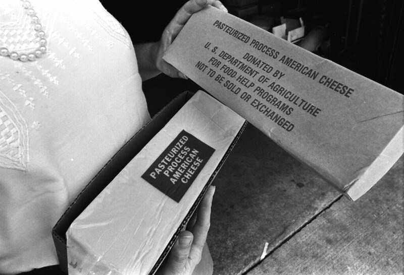 A black and white photo of a person holding a block of cheese labeled Pasteurized Process American Cheese