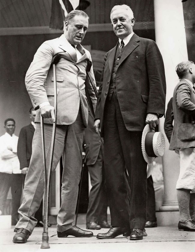 FDR with crutches standing with John Davis on the front terrace at Springwood, 1927. Valet Leroy Jones stands in the background at the far left.