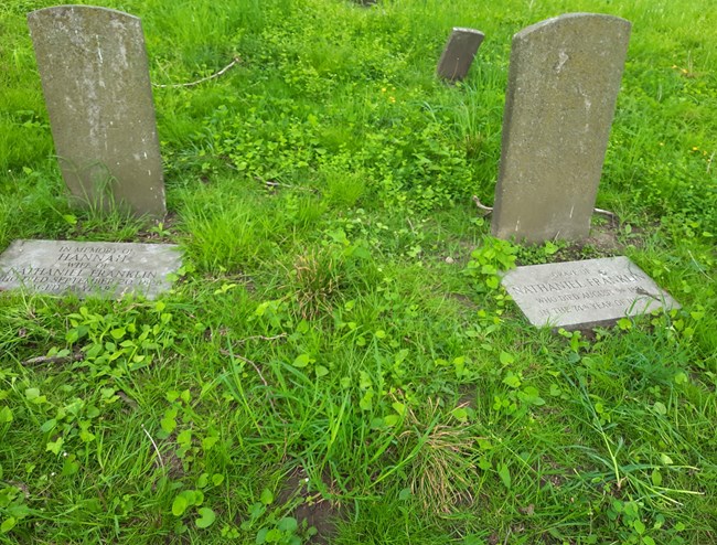 Two light grey gravestones, with inscriptions, in a grassy patch.