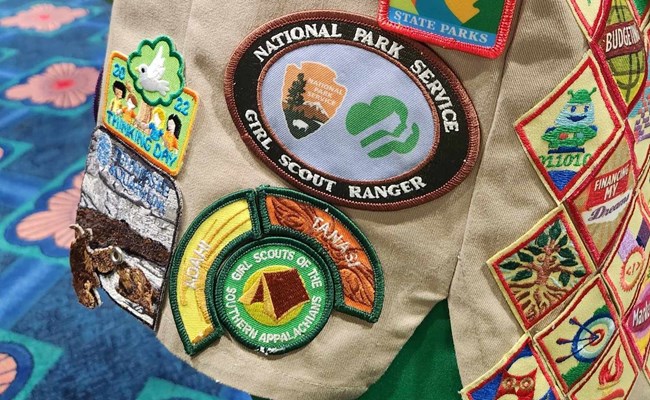A display of various colorful Girl Scout patches on a khaki vest.