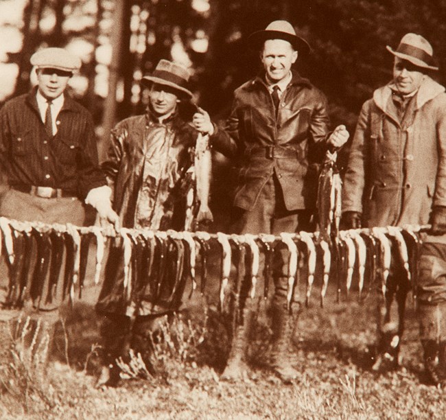 Four men stand behind of string of fish showing off their catch.