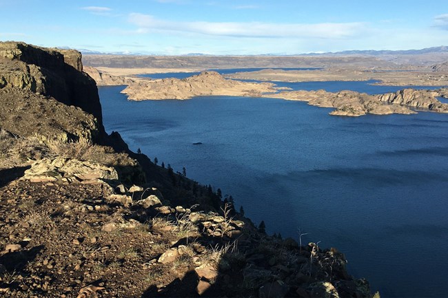 Color photo of a large lake surrounded by steep rocky outcroppings.