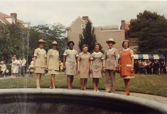 Seven women standing in a line modeling different beige uniforms.
