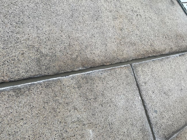 Close up photograph of grey granite blocks with a fresh pass of mortar in the seam.