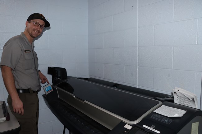 A park ranger works on printing equipment in an office setting.