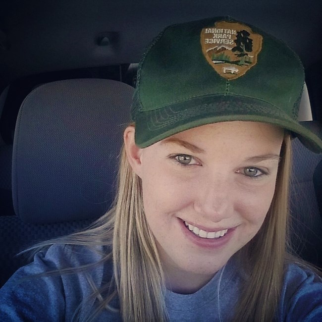 a selfie of a young woman in a park service ball cap