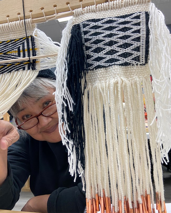 Woman smiles at camera while holding a woven item to the side.