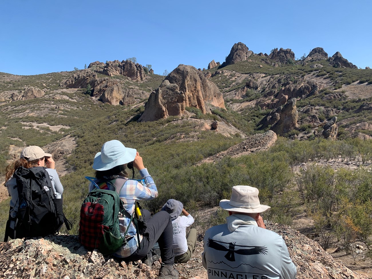 People looking through binoculars into vast arid landscape dotted with rocky cliffs—aka, ideal falcon nesting habitat—in the distance