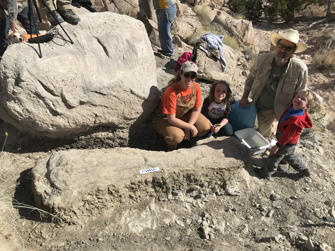 a family of three squats next to a large fossil