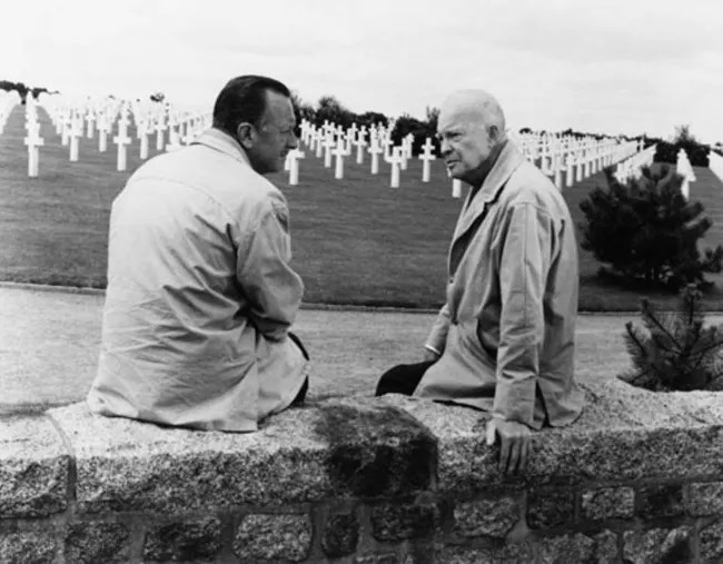 Ike and Cronkite 1963 A black and white image of two men sitting on a stone wall